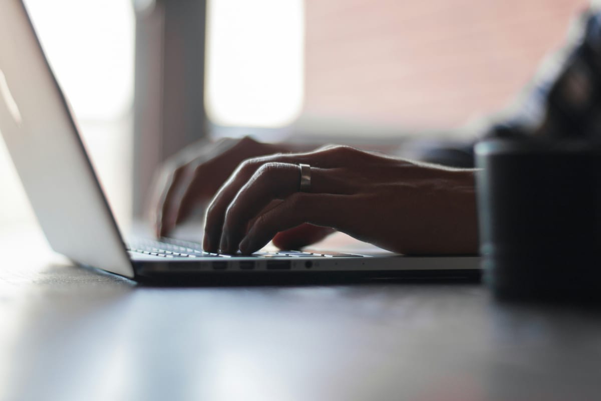 Mãos digitando em um notebook sobre uma mesa